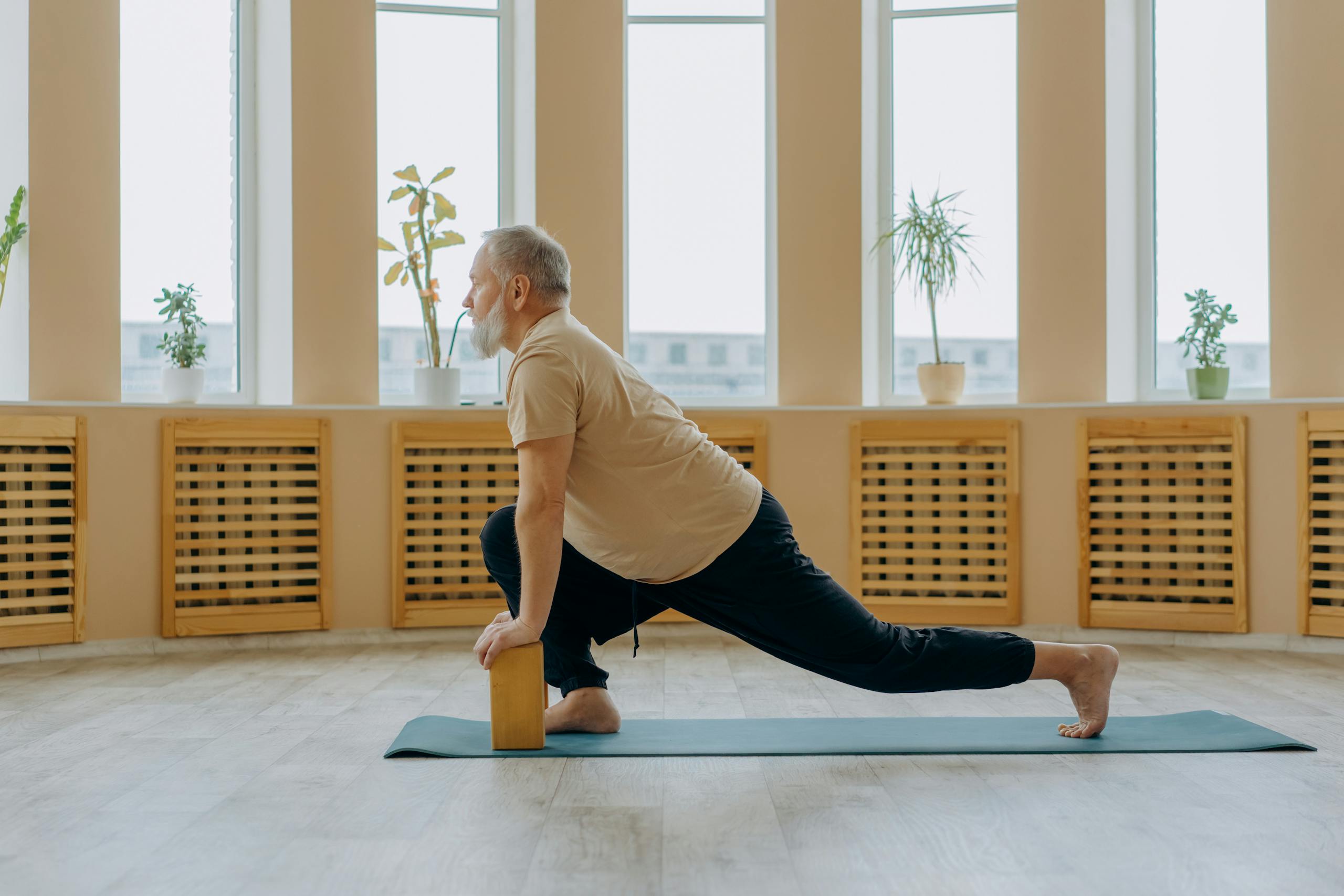 Elderly man stretching on a yoga mat using a wooden block, promoting fitness and a healthy lifestyle.